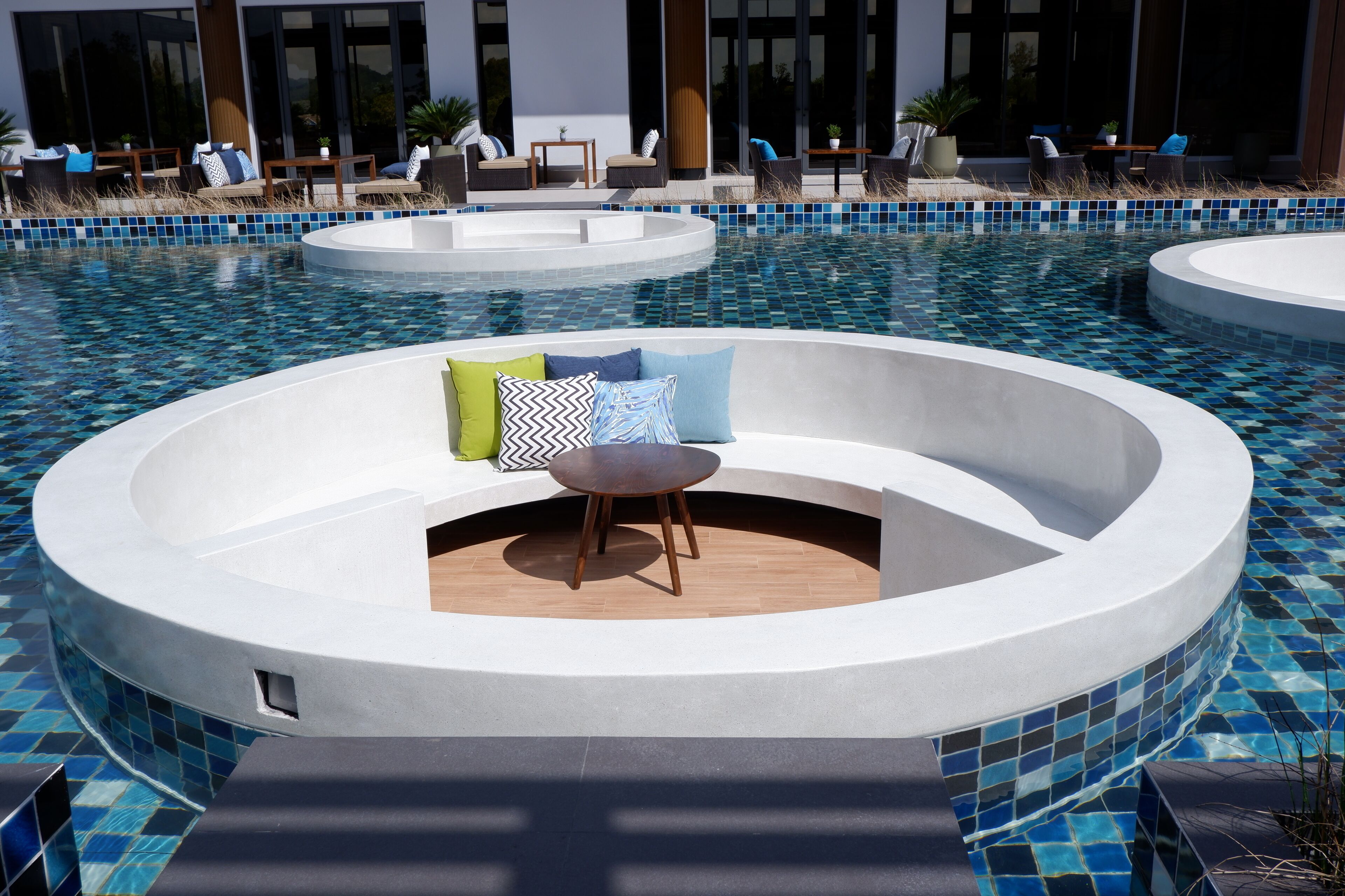 Un espace piscine moderne avec un coin salon circulaire, des chaises longues et une petite table.