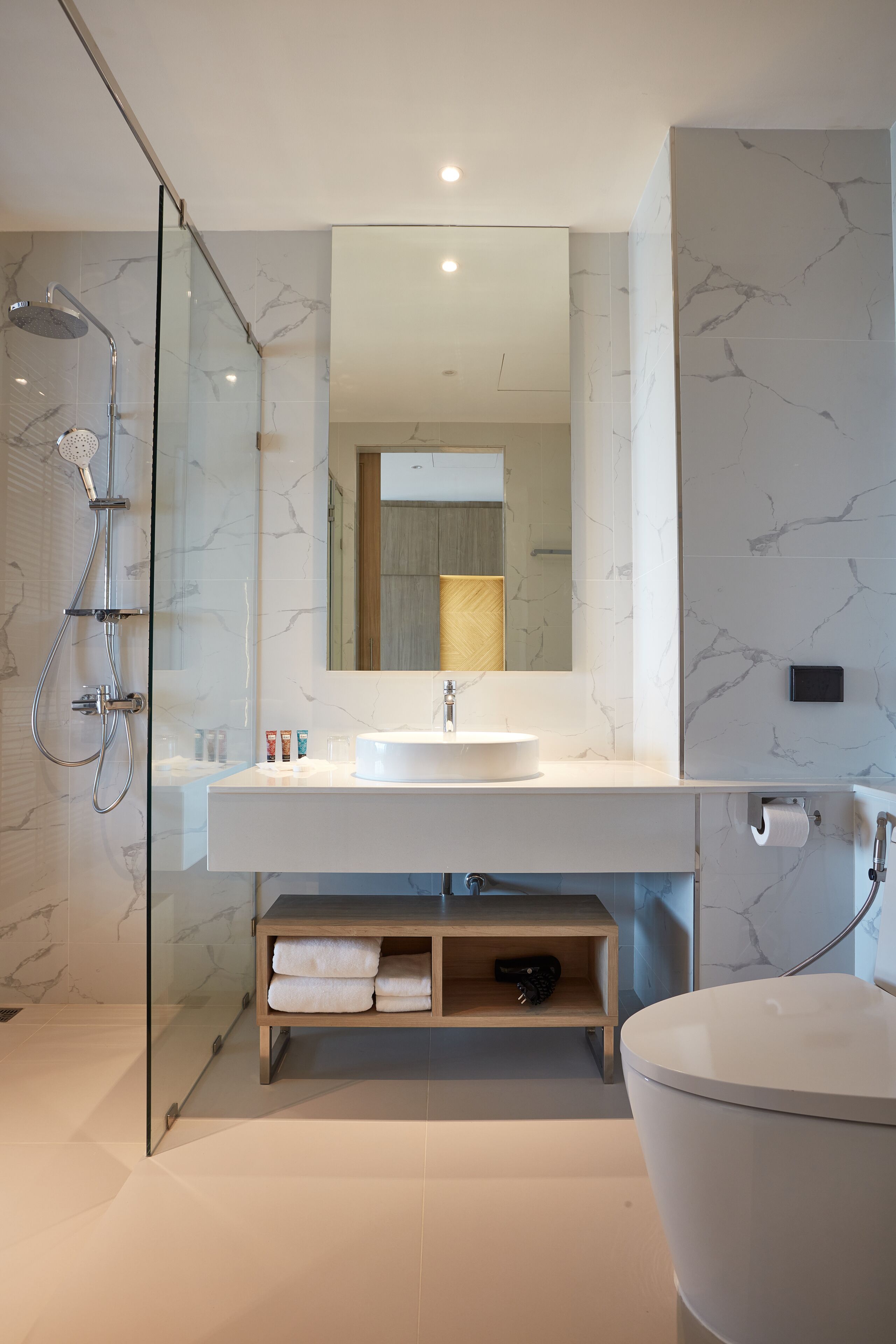 Ein modernes Badezimmer mit einer gläsernen Duschkabine, einem weißen Waschbecken mit Marmorablage, einem großen Spiegel und einer freistehenden Badewanne.