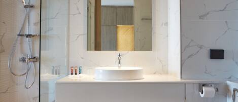 Une salle de bain moderne avec une douche à parois de verre, un lavabo blanc avec un pare-éclaboussures en marbre, un grand miroir et une baignoire sur pieds.