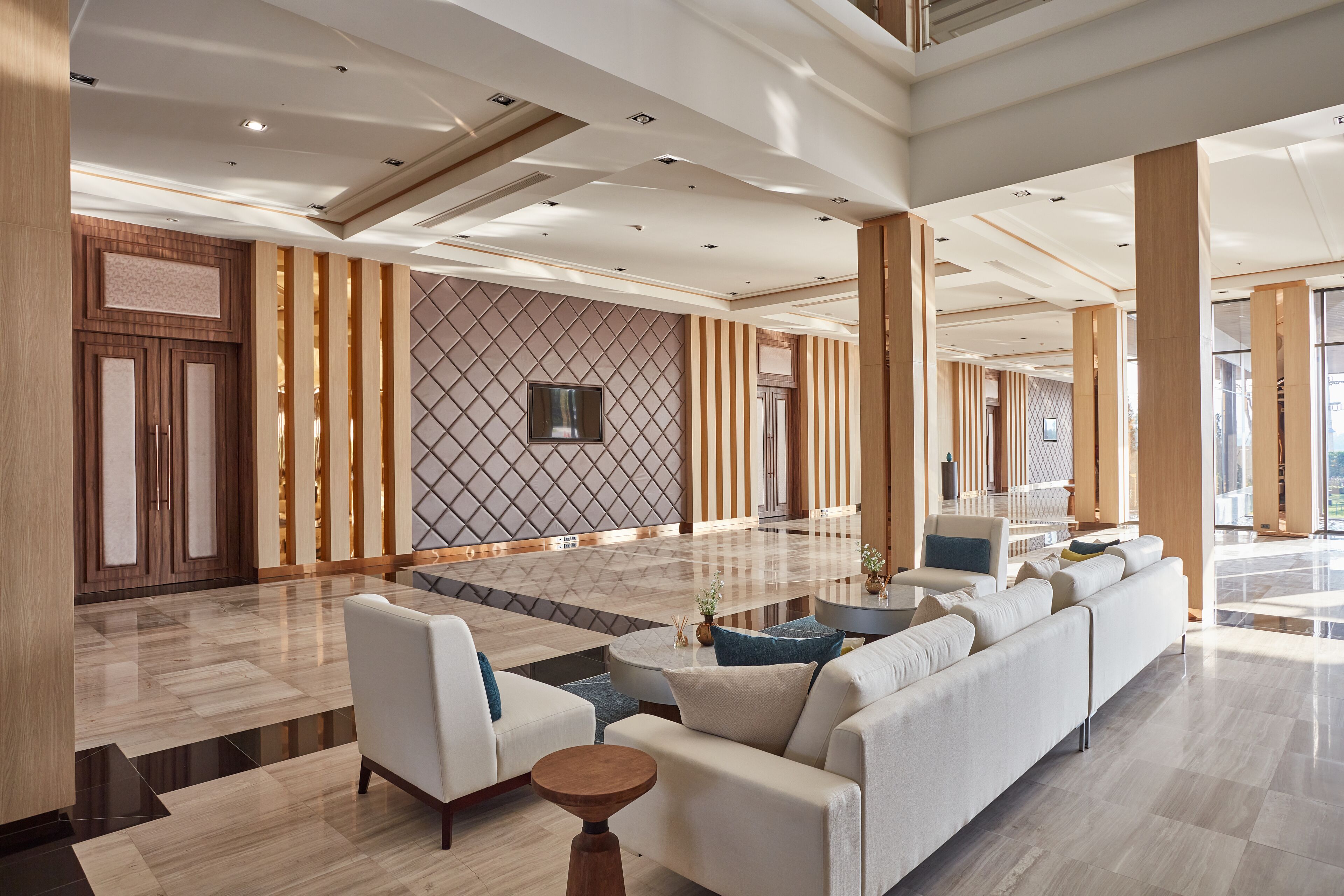 Eine geräumige Lobby mit modernem Design, ausgestattet mit einer großzügigen Sitzecke, bequemen Sofas, einem Couchtisch, einer Wand mit Muster und einem großen Fenster, das für natürliches Licht sorgt.