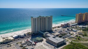 Un grand hôtel avec vue sur la plage, un parking et une jetée en arrière-plan.