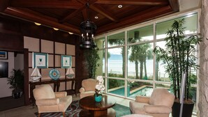 Un salon spacieux doté d’une grande fenêtre donnant sur une piscine, de sièges confortables et d’un vase décoratif posé sur une table basse en bois.