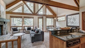 A spacious living area with a fireplace, a stone accent wall, a gray sofa with colorful pillows, and a large window overlooking trees. - Luxury 4 Bed Pines Townhome Amongst The Peace And Quiet 4 Bedroom Townhouse by RedAwning (Avon)
