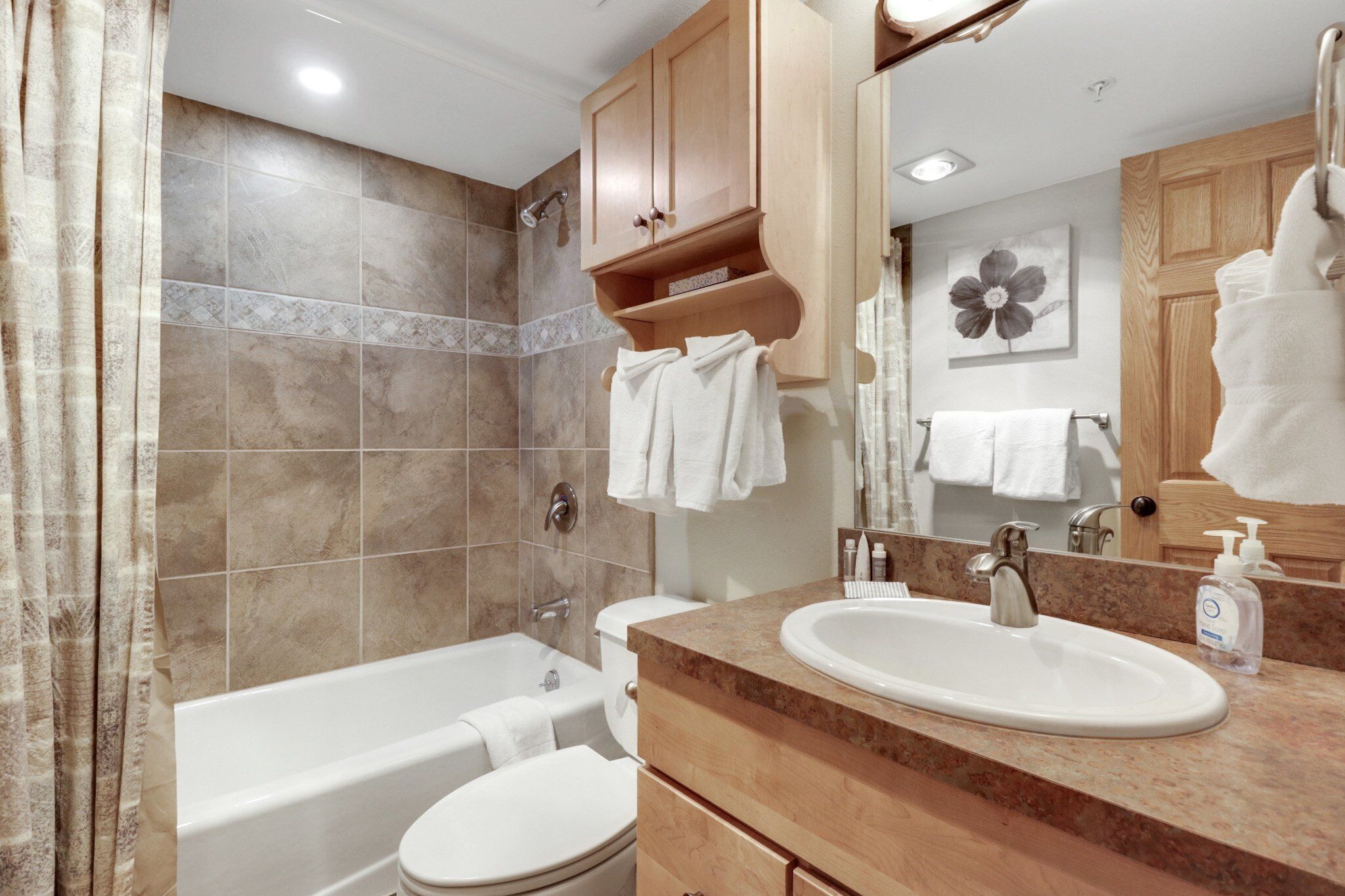 A modern bathroom with a bathtub, toilet, and sink. There are wooden cabinets above the sink and a large mirror.