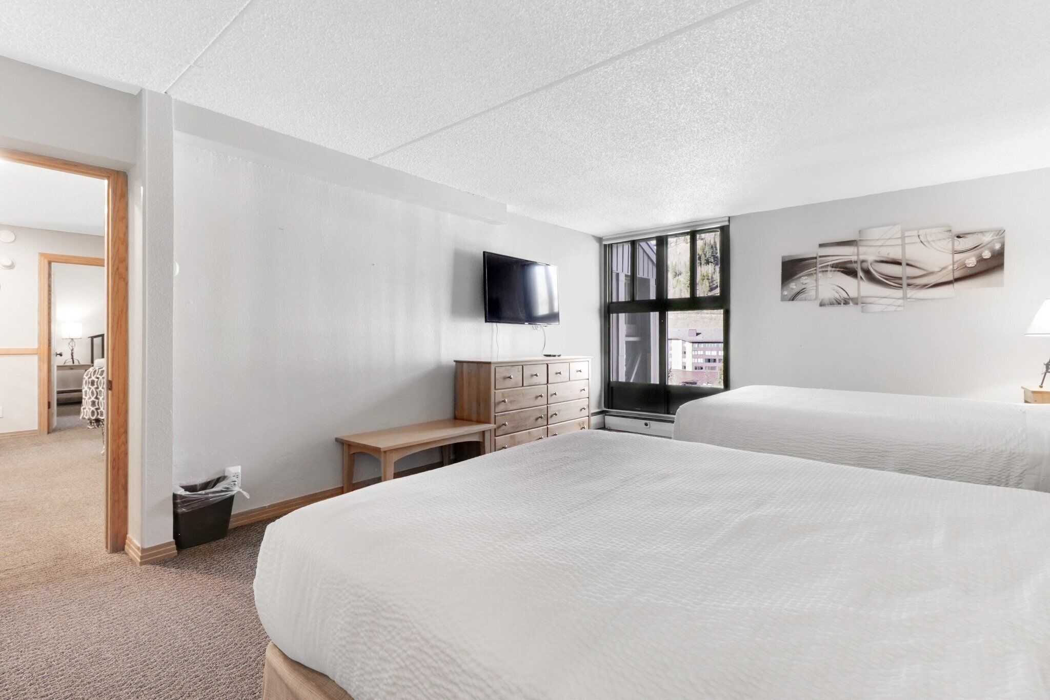A hotel room with two beds, a TV, a desk, a dresser, and a window with a view.