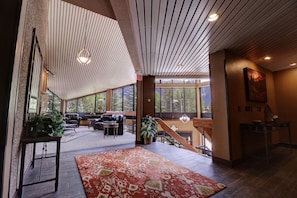 Relax in a spacious living area with a leather sofa, coffee table, and dining table, surrounded by a large rug and natural light pouring in through large windows.