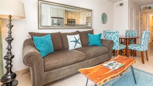 Een woonkamer met een bruine bank, teal kussens, een houten salontafel en gestreept beklede stoelen.