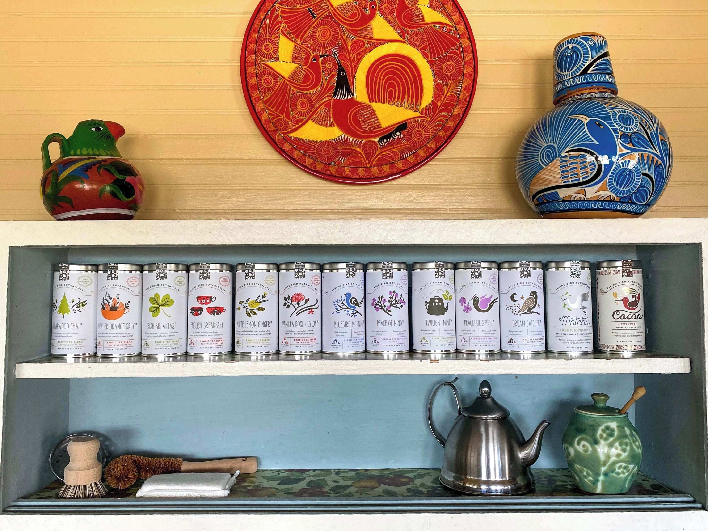 Een plank met theedozen, een metalen theepot, een keramieken pot en decoratieve objecten.