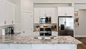 A modern kitchen with white cabinetry, a granite countertop, stainless steel appliances, and a built-in island with bar stools.