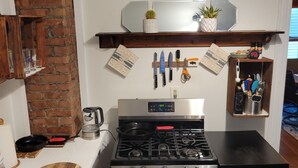 A kitchen with a brick wall, a stainless steel stove, a wooden countertop, and a shelf with kitchen utensils.