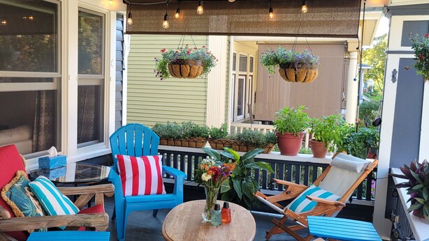 A covered outdoor seating area with wooden furniture, hanging planters, and string lights.