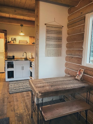 A rustic cabin interior with a wooden dining table, bench, and a hanging tapestry. - Timberwolf Cabin (at 9,000 ft) (Florissant)