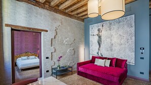 Una habitación con una cama, un sofá rojo, una mesa de mármol y un cuadro abstracto grande en la pared.