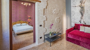 Una habitación con una cama, un sofá rojo, una mesita con una planta y una pared con un cuadro abstracto grande.