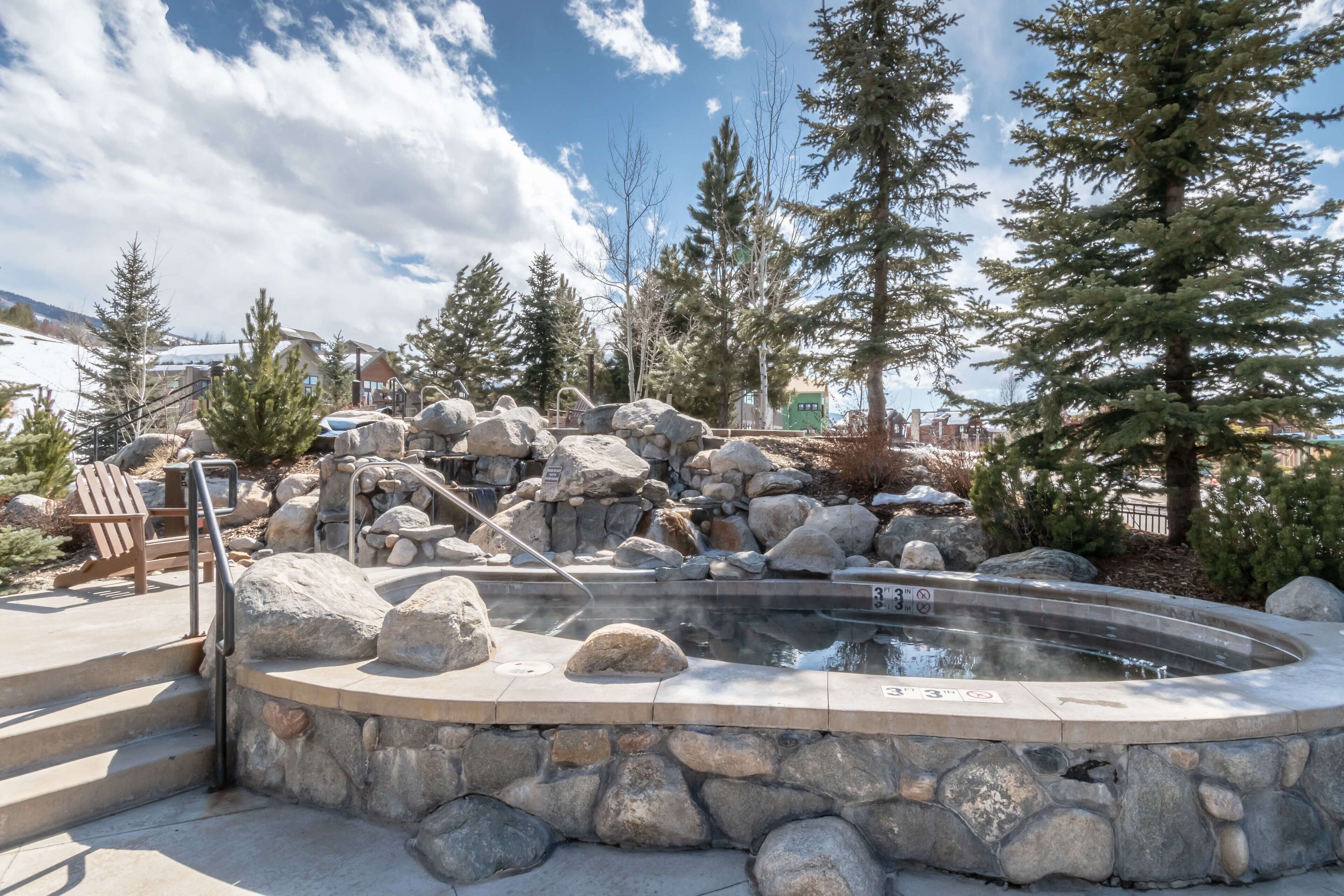 Un jacuzzi rodeado de rocas y árboles, con una silla y escalones que lo conducen.