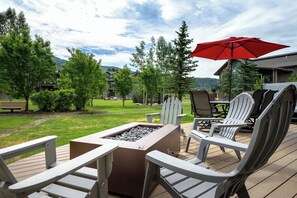 Eine Terrasse im Freien mit Adirondack-Stühlen, einer Feuerstelle und einem roten Sonnenschirm.