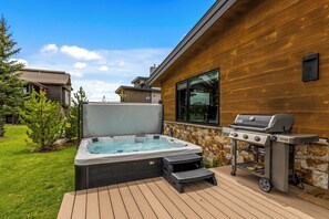 Ein Whirlpool, ein Grill und eine Terrasse mit einem Holzhaus und einer Steinmauer im Hintergrund.