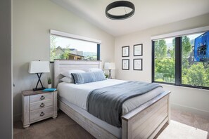 Ein Schlafzimmer mit einem Bett, Nachttischen, einem Fenster und gerahmten Bildern an der Wand.