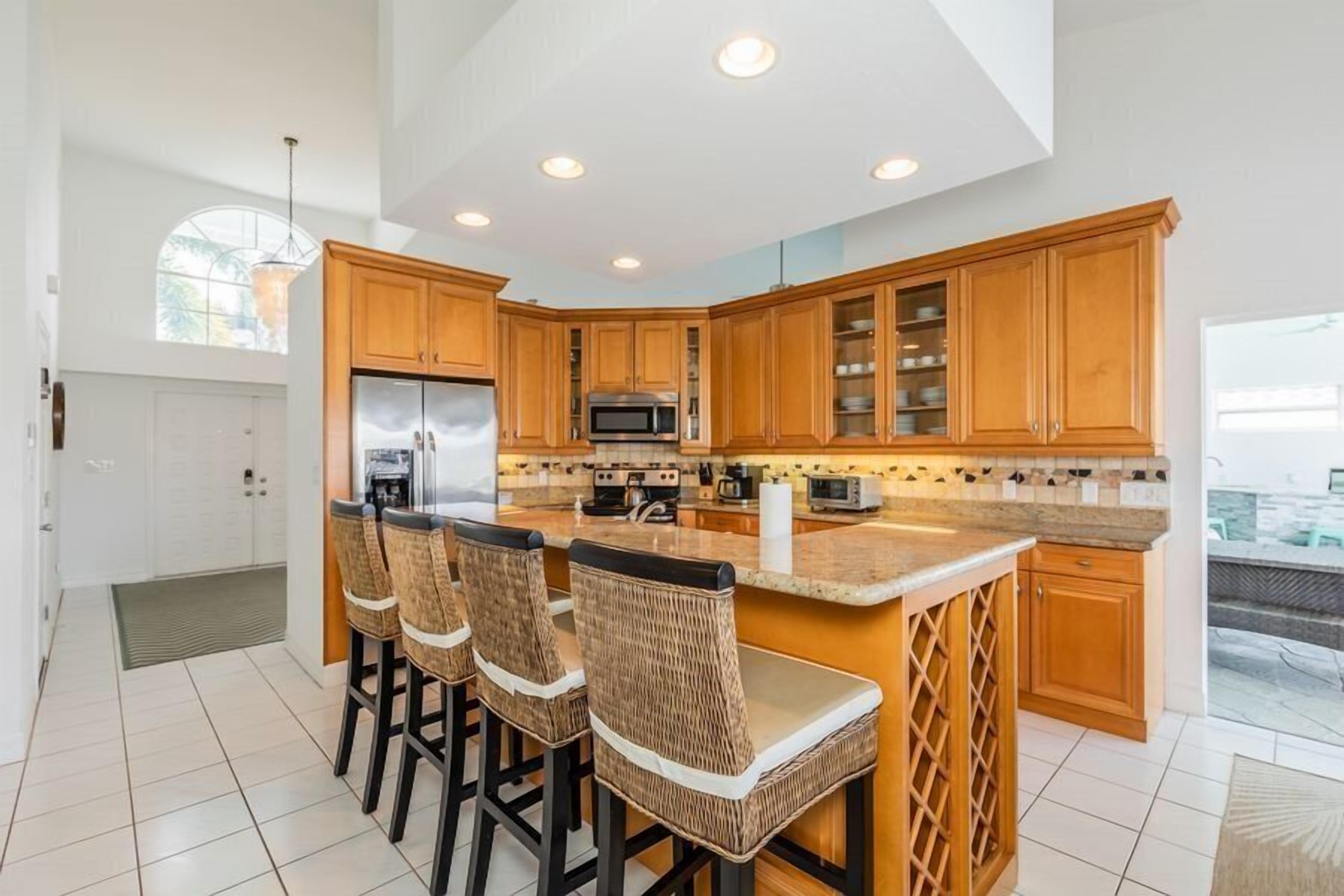 A modern kitchen with wooden cabinets, a central island with bar stools, a stainless steel refrigerator, and a microwave.