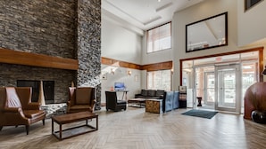 Eine geräumige Lobby mit Steinwand, Ledersesseln, einem Holztisch und einem großen Spiegel.