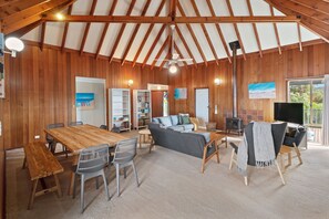 Amplia sala de estar con techo de madera, un sofá grande, una mesa de comedor con sillas y una chimenea.