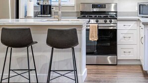 Una cocina moderna con un refrigerador de acero inoxidable, un horno empotrado, una estufa a gas, un extractor de acero inoxidable y dos taburetes de bar.
