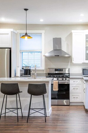 A modern kitchen with a stainless steel refrigerator, a built-in oven, a gas stove, a stainless steel range hood, and two bar stools. - Fremont Haven: Bright, Comfortable & Central (Seattle)