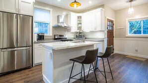 A modern kitchen with white cabinetry, stainless steel appliances, and a central island with bar stools. - Fremont Haven: Bright, Comfortable & Central (Seattle)