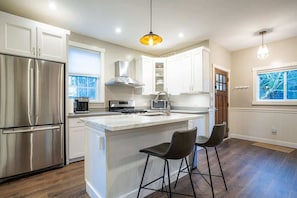 Una cocina moderna con armarios blancos, electrodomésticos de acero inoxidable y una isla central con taburetes de bar.
