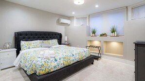 A modern bedroom with a large bed, bedside tables, an air conditioner, and a window with plants. - Fremont Haven: Bright, Comfortable & Central (Seattle)