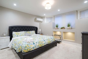 Un dormitorio moderno con una cama grande, mesitas de noche, aire acondicionado y una ventana con plantas.