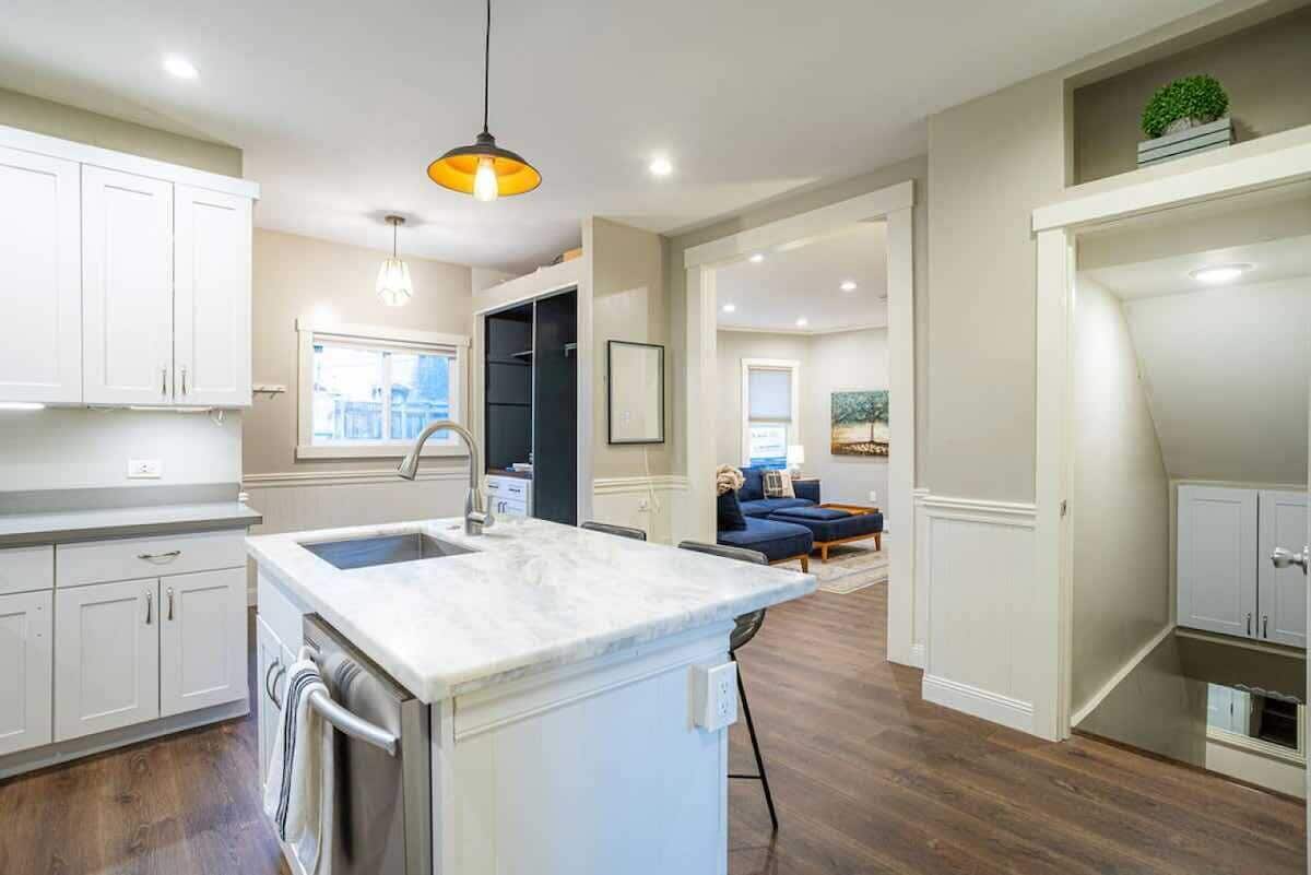 A modern kitchen with white cabinets, a marble island, and a pendant light.