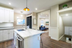 Une cuisine moderne avec des meubles blancs, un îlot en marbre et un luminaire suspendu.