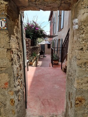 A narrow alleyway with stone walls, a small table with chairs, and potted plants.