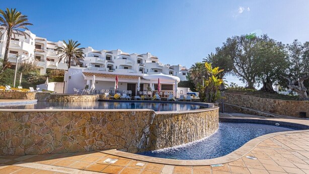Een resort met een zwembad, witte gebouwen en palmbomen.