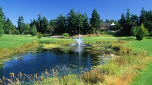 A golf course with a pond, trees, and a building in the background.