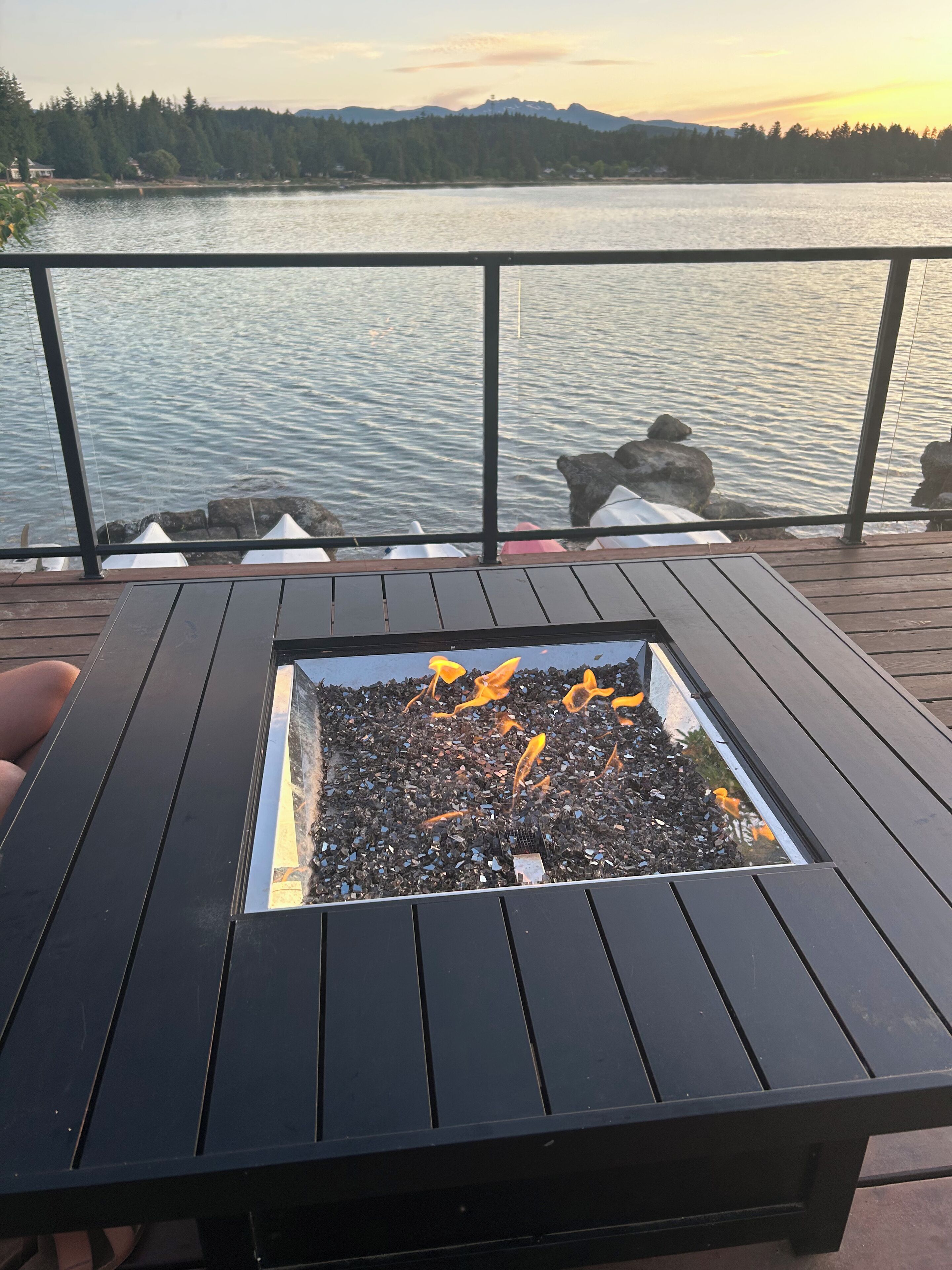 Une table en métal noir avec un foyer carré au centre, entourée d’une terrasse en bois.