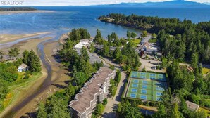 An aerial view of a coastal residential area with houses, a tennis court, and a beach.