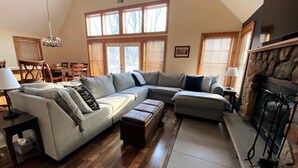 A living room with a sectional sofa, a fireplace, wooden flooring, and large windows.