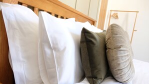 Un lit avec des oreillers blancs et bruns, une tête de lit en bois et une table de chevet en bois sur laquelle se trouve un objet blanc.