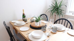 Une table à manger dressée avec de l’assiette, des bols et des verres blancs, une bouteille de champagne et une plante en pot.