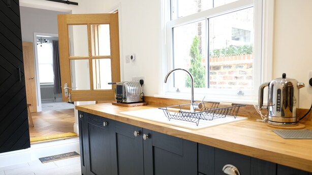 Une cuisine moderne avec des meubles de couleur sombre, un plan de travail en bois, un grille-pain, une bouilloire et une fenêtre donnant sur l’extérieur.