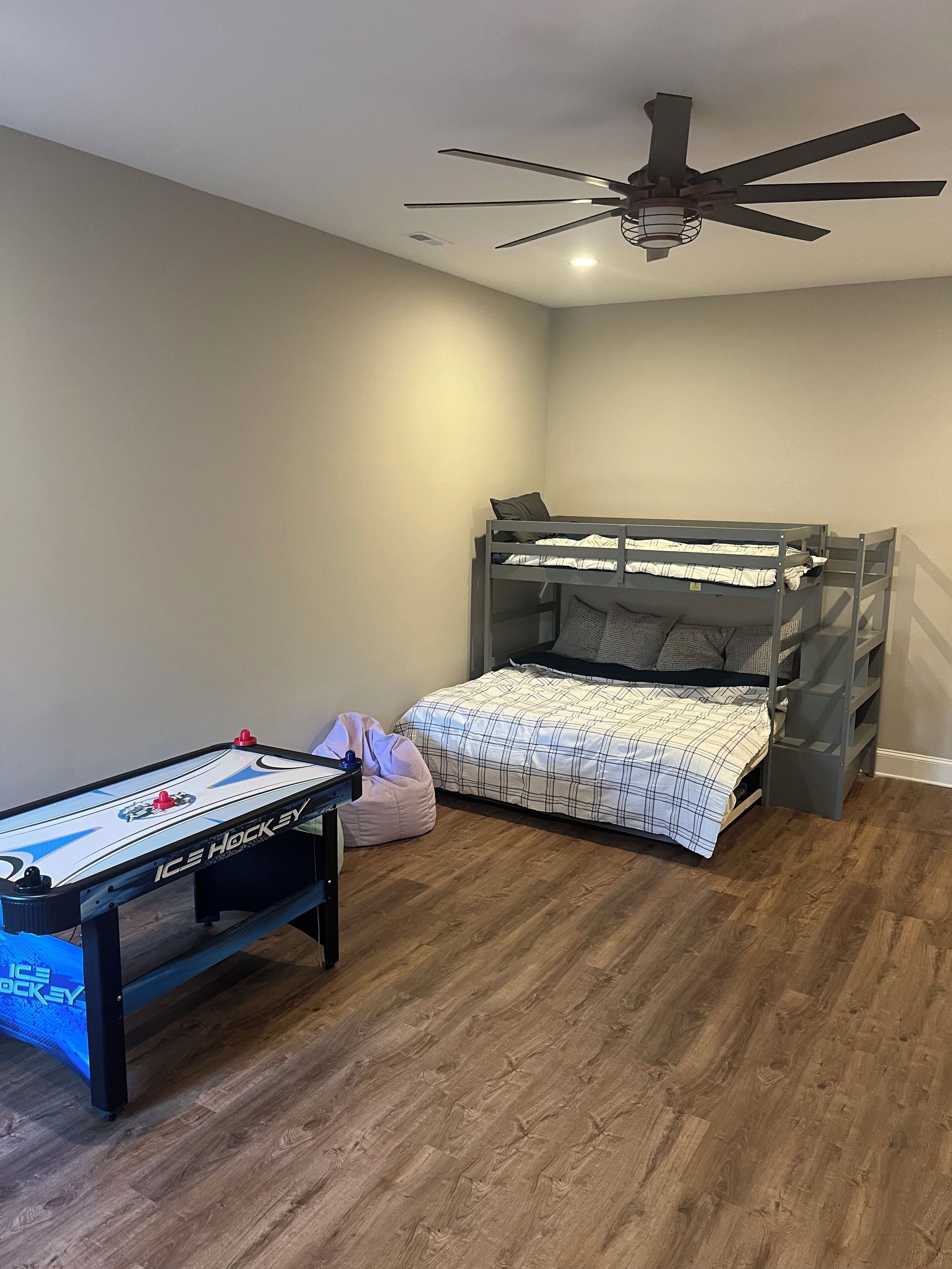 A bedroom with a bunk bed, a ceiling fan, a small table with a hockey table, and a bean bag chair.