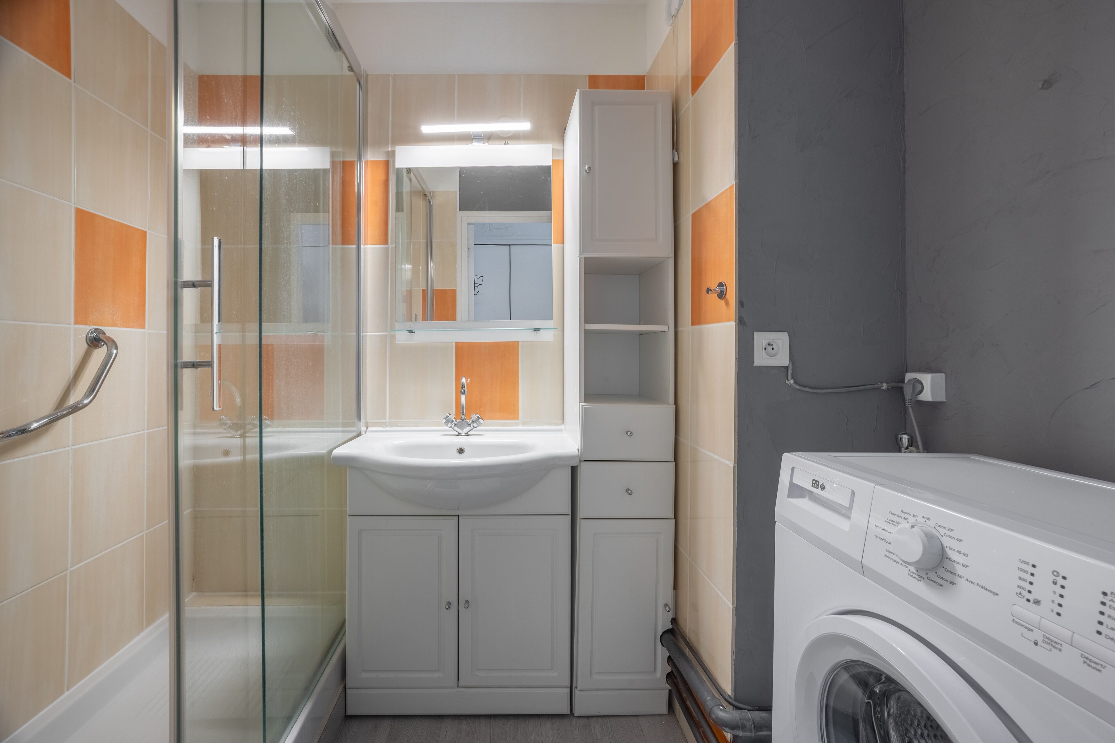Une salle de bain compacte avec une douche à parois de verre, un lavabo, un miroir et un lave-linge.