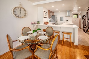 A dining area with a round glass table, six chairs, and a wall clock.