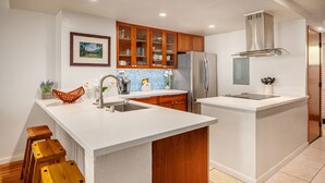 Une cuisine moderne avec des meubles en bois, un réfrigérateur en acier inoxydable et un plan de travail blanc.