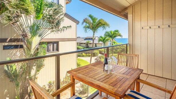 Une table et des chaises en bois sur un balcon donnant sur l’océan et les palmiers.