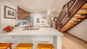 Une cuisine moderne avec un îlot central, des tabourets en bois et un escalier en bois.