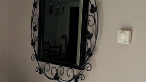 Ein Badezimmer mit einem schwarzen, verzierten Spiegel, einem Glastischchen mit dekorativem Metallgestell und einem Handtuchhalter mit Handtuch.