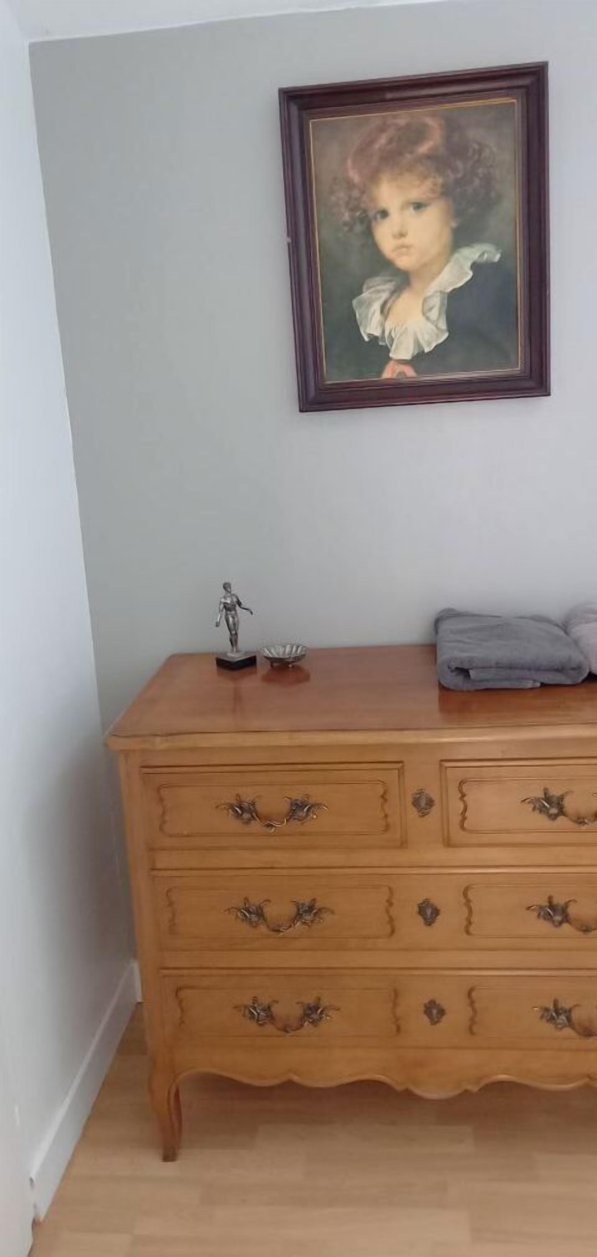 A wooden dresser with ornate handles, a framed portrait on the wall, and a small statue on the dresser.